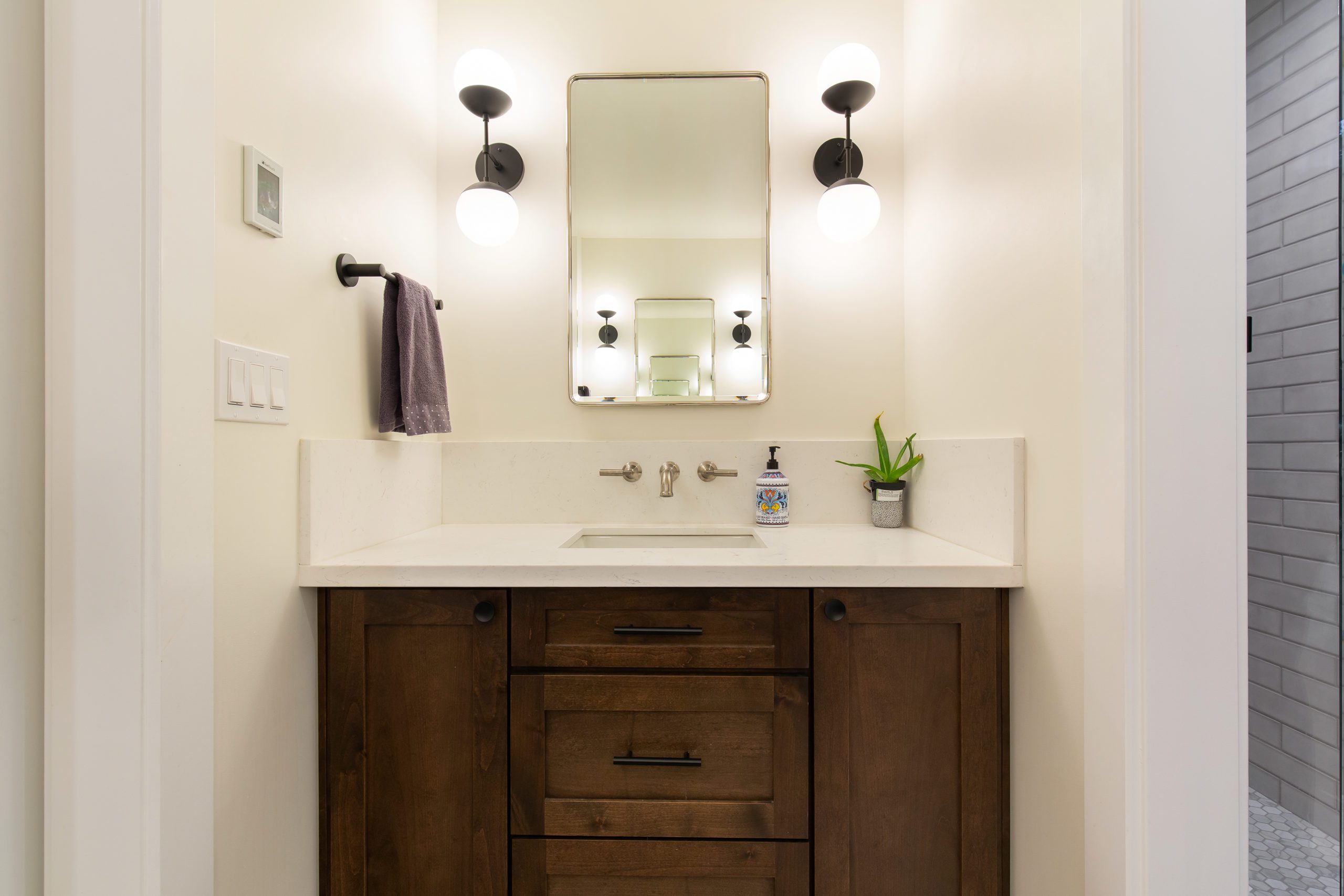 Remodeled bathroom counter with dark cabinetry, white and black light fixtures, white counters and an aloe plant