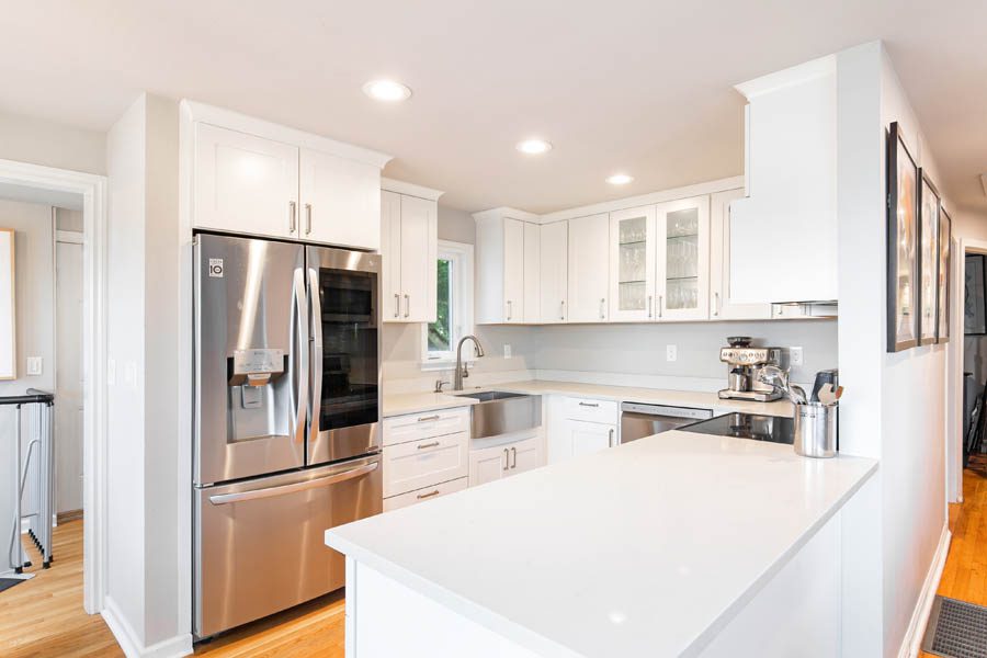Small white kitchen with white cabinets and stainless steel fridge