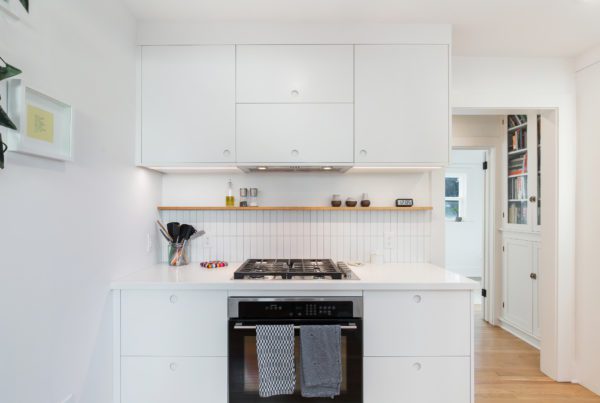 All white mini kitchen remodel with white cabinetry, white walls, white tile, an oven, other appliances and wooden flooring