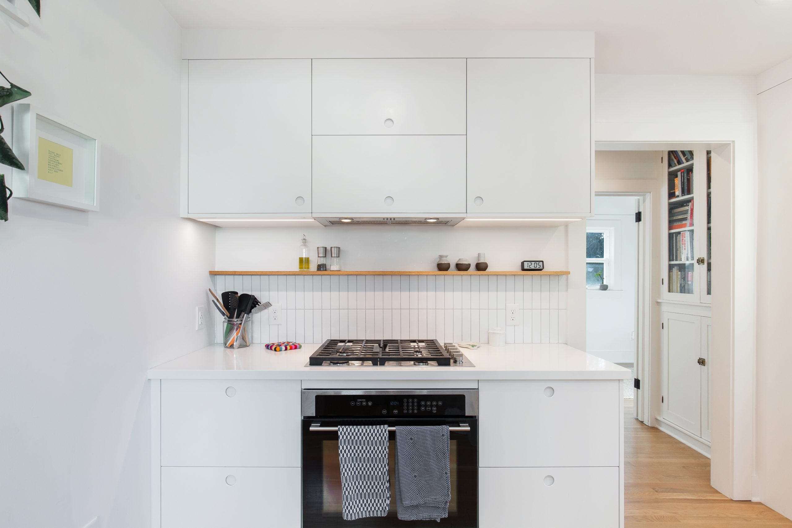 All white mini kitchen remodel with white cabinetry, white walls, white tile, an oven, other appliances and wooden flooring