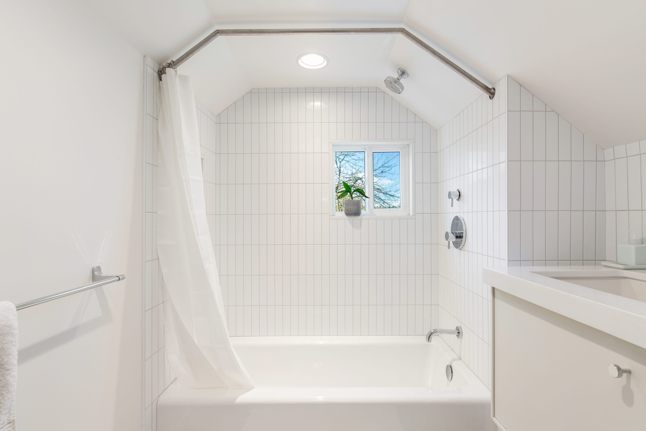 All white and bright renovated bathroom with white tile, white walls, white counters and minimal decorations