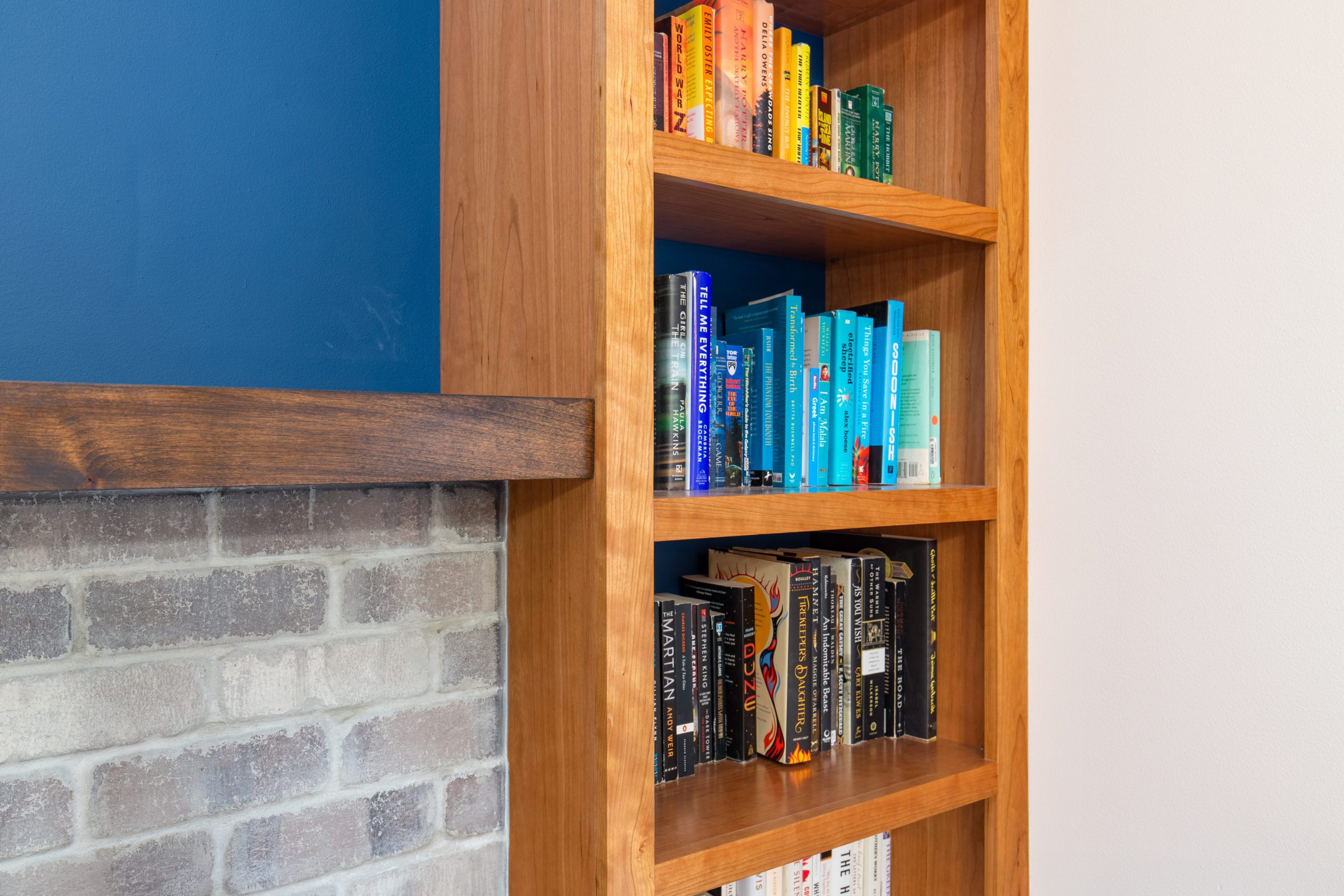 Book shelf built into a blue wall with a fireplace built next to it with wooden and stone details