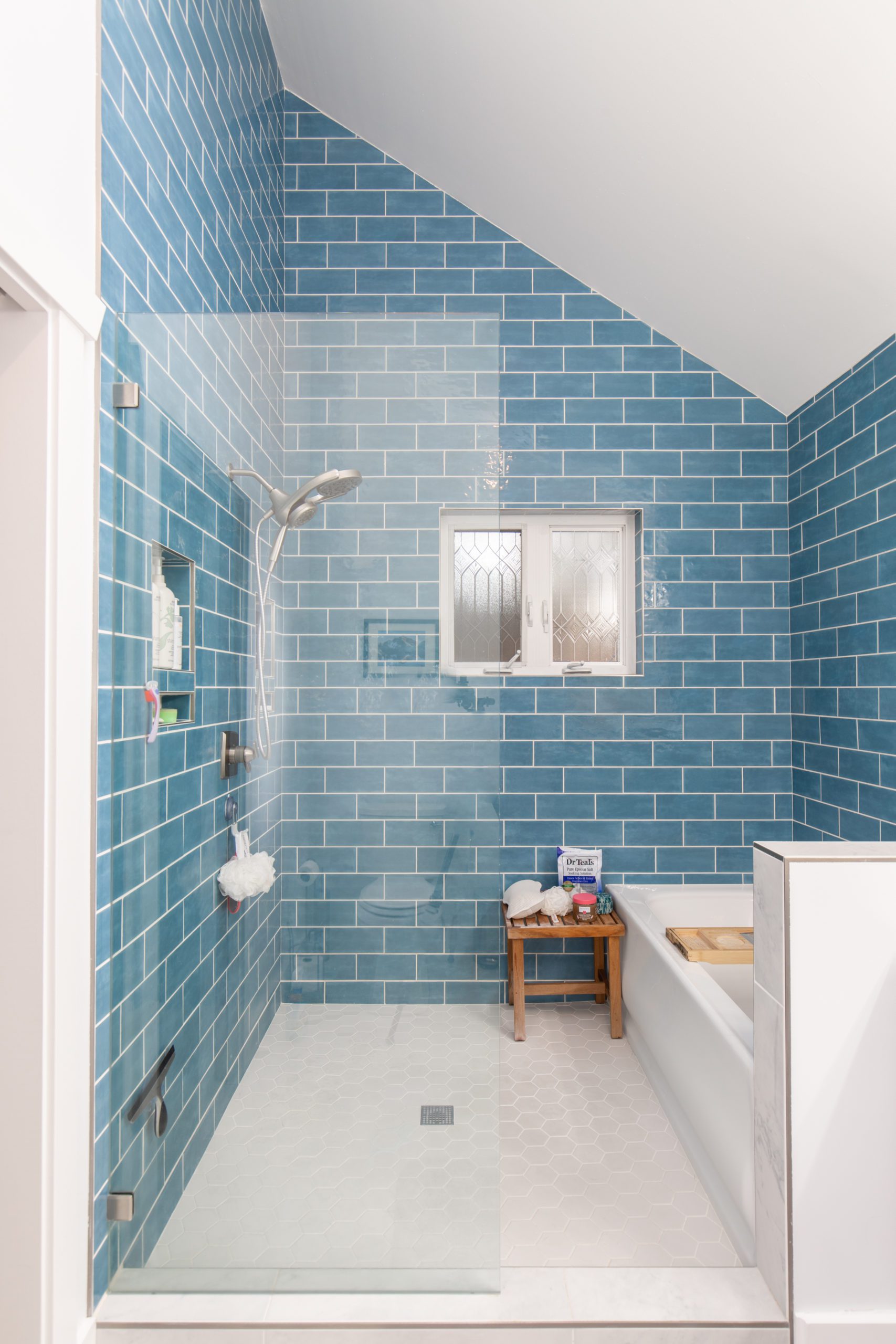 Renovated large open concept shower with teal tile backsplash walls, white tile flooring, renovated appliances