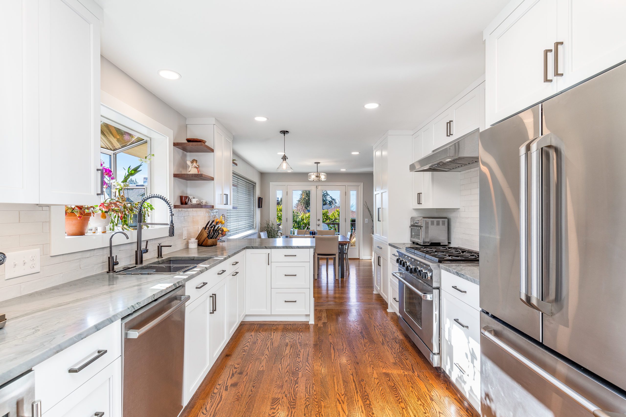 Kitchen remodel with wooden floors, white cabinetry, marble counter tops, new silver appliances and large window