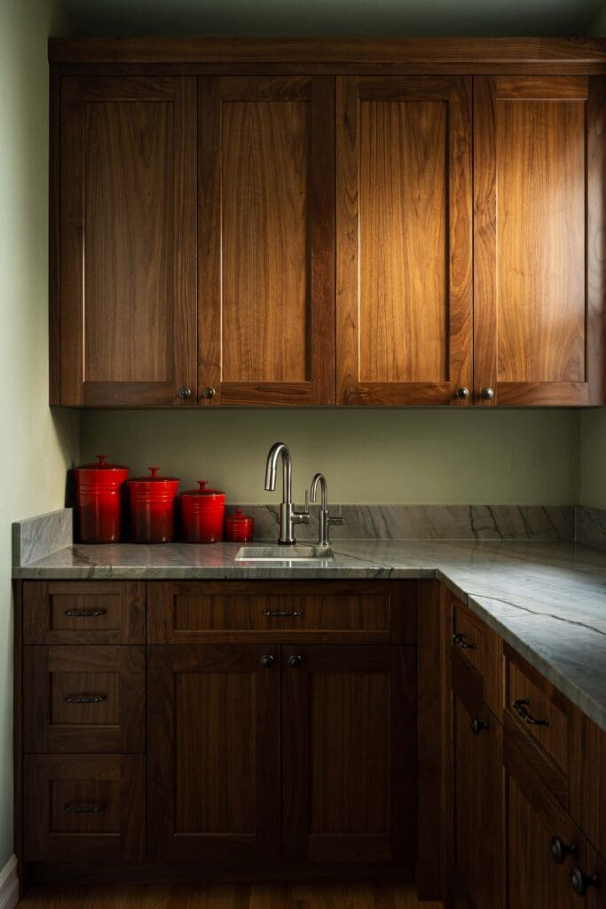 HAAS-Seattle-Pantry-Remodel-11 (2) A kitchen featuring Seattle custom cabinets in dark wood, a small sink with a silver faucet, marble countertops, and several red canisters placed on the counter.