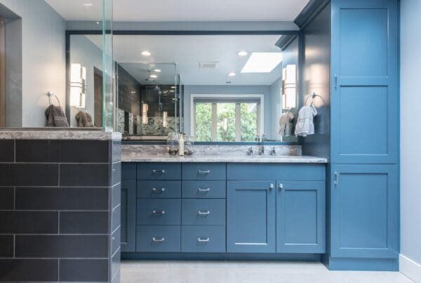 Modern Normandy Park Mid Century Modern bathroom with blue cabinets, marble countertop, large mirror, glass shower, black tile, and two wall-mounted lights. Towels hang by the window as natural light fills the space.