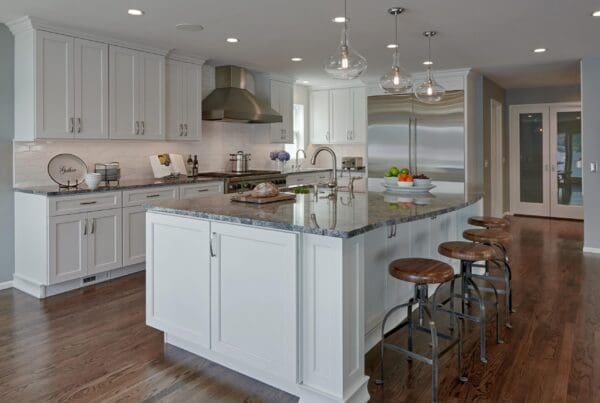 Modern Seattle Waterfront Kitchen Remodel featuring white cabinets, a large marble island with wooden stools, stainless steel appliances, pendant lights, hardwood floors, and stylish kitchen decor.