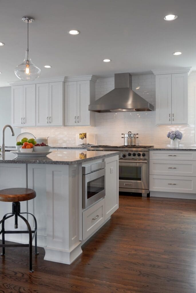 DSC9846-1-scaled Modern Seattle Waterfront Kitchen Remodel with white cabinets, stainless steel appliances, an island with microwave, fruit bowl, wooden stool, and hardwood floors under bright recessed lighting.