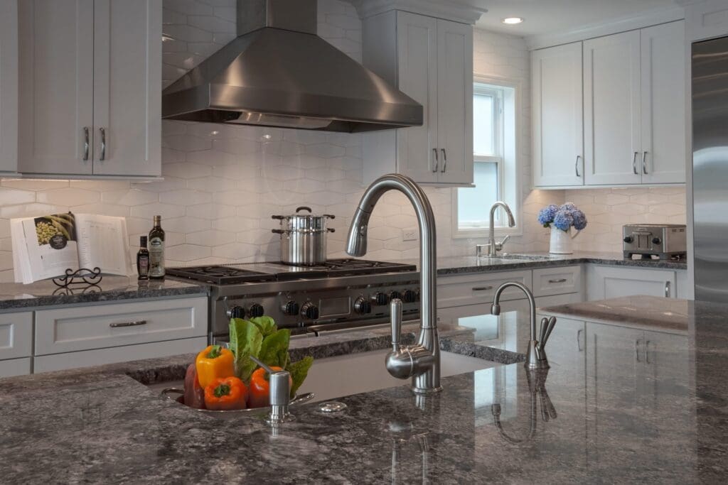DSC9871-1-scaled Modern kitchen with gray granite countertops, stainless steel appliances, and fresh vegetables in the sinkāa bright Seattle Waterfront Kitchen Remodel featuring white cabinets and blue flowers by the window.