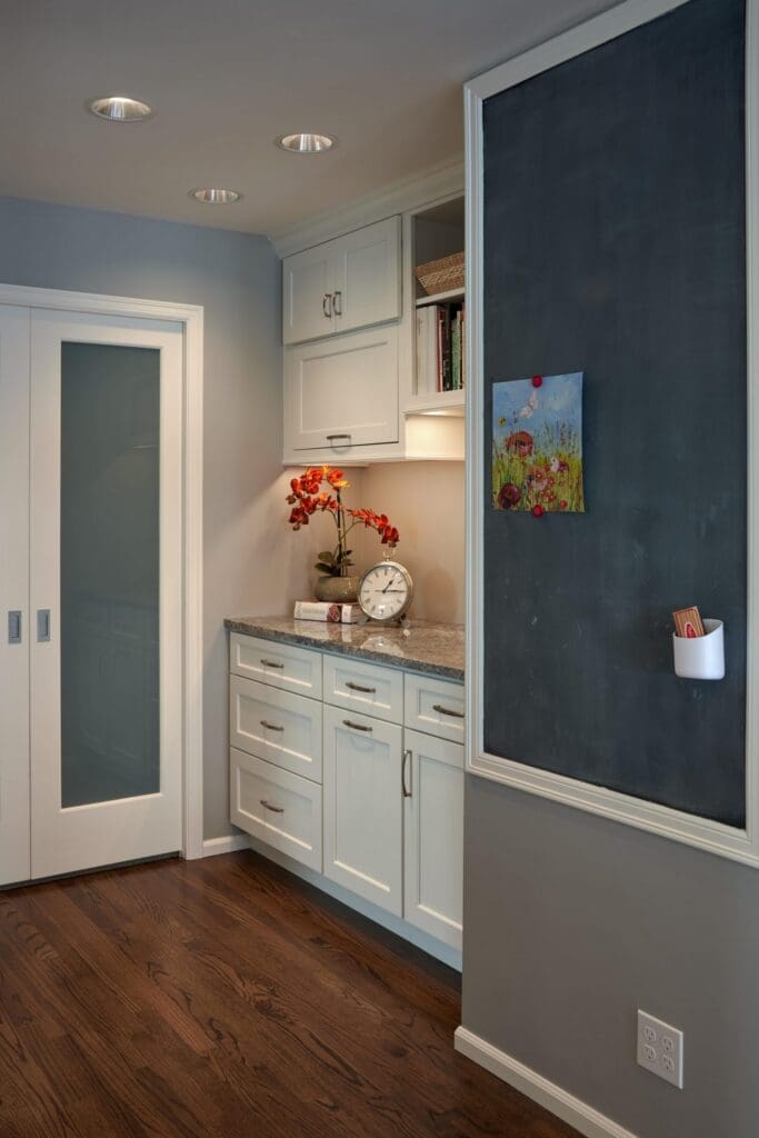 DSC9876a-1-scaled A kitchen corner from a Seattle Waterfront Kitchen Remodel features white cabinets, granite countertop, red flowers, hardwood floors, sliding doors, and a chalkboard wall with art and a cup holding chalk.