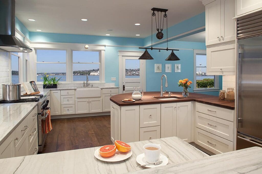 MG_5787-1 Bright Queen Anne Kitchen Remodel with white cabinets, marble counters, wood floors, farmhouse sink, pendant lights, and large windows with a water view. Grapefruit and coffee sit on the counter.