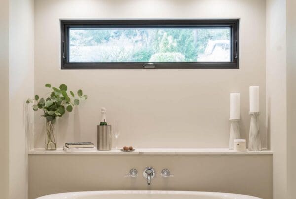 Modern Mercer Island Bathroom Remodel featuring a white oval bathtub, dark towel, and decorative shelf with candles, plants, and a bottle. A window above and a starburst light fixture complete the look.