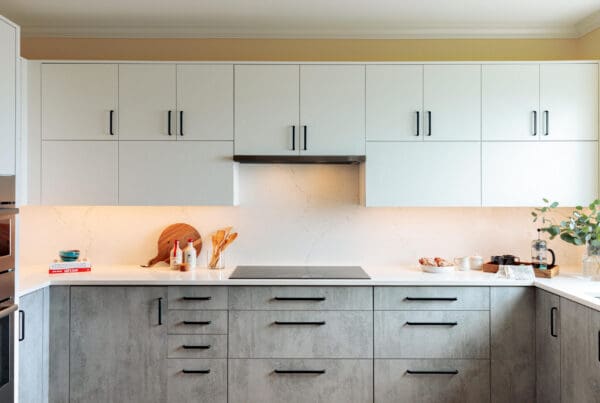 West Seattle Bright and Modern Kitchen Remodel featuring white upper cabinets, gray lowers, black handles, a built-in cooktop, wood floors, and minimalist decor with cutting boards, utensils, and greenery on the countertop.